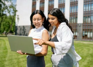 9 Reasons Social Media Algorithms Reward Meaningful Comments Two women happily collaborate on a laptop outside an office building.
